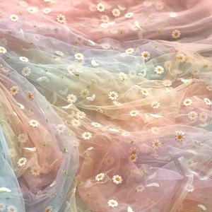 May include: A sheer, rainbow-coloured fabric with embroidered white daisies. The fabric is soft and delicate, perfect for crafting or adding a touch of whimsy to any project.