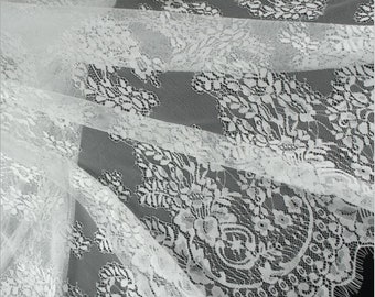 May include: Close-up of white lace fabric with floral patterns. The delicate lace is layered, creating depth and texture. The intricate design features detailed floral motifs, perfect for bridal wear or decorative projects.