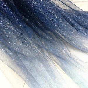 Peut inclure: Un tissu de tulle bleu et blanc ombré avec des paillettes incrustées dans le tissu.