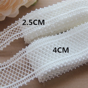 May include: Two rolls of white lace trim, one 2.5 cm wide and the other 4 cm wide. The lace has a delicate diamond pattern.