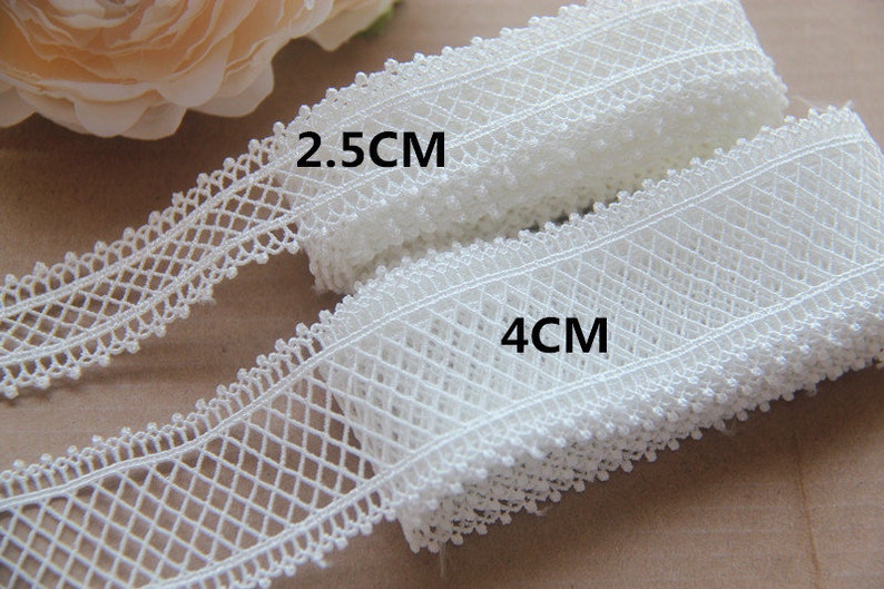 May include: Two rolls of white lace trim, one 2.5 cm wide and the other 4 cm wide. The lace has a delicate diamond pattern.