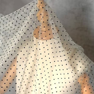 Puede incluir: Tela blanca transparente con lunares negros. La tela está drapeada sobre un maniquí.