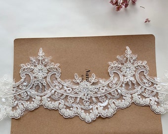 May include: White lace trim with a floral design and silver sequins. The lace is delicate and intricate, with a scalloped edge.