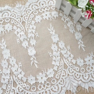 K&ouml;nnte beinhalten: Wei&szlig;e Spitzenborte mit zartem Blumenmuster. Die Spitze hat einen gewellten Rand und ist perfekt, um jedem Projekt einen Hauch von Eleganz zu verleihen.