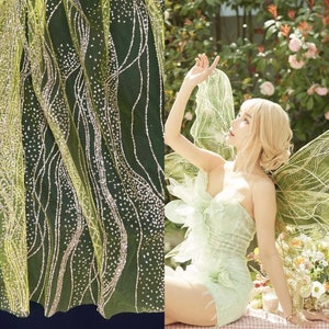 Op de afbeelding: Een groene tule stof met zilveren glitteraccenten. De stof heeft een vloeiende, golvende print.