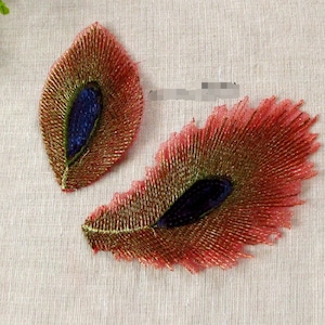 Peut inclure: Deux plumes de paon brodées en rouge, vert et bleu. Les plumes sont détaillées avec du fil doré et ont une finition brillante.