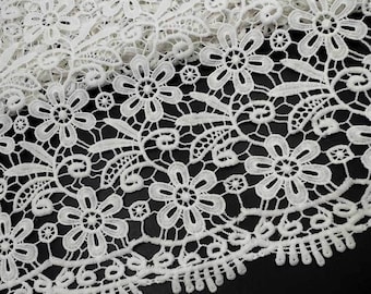 May include: White lace fabric with a delicate floral pattern. The lace has a scalloped edge and is perfect for crafting projects.