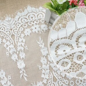 K&ouml;nnte beinhalten: Wei&szlig;e Spitzenborte mit zartem Blumenmuster. Die Spitze hat einen gewellten Rand und ist perfekt, um jedem Projekt einen Hauch von Eleganz zu verleihen.