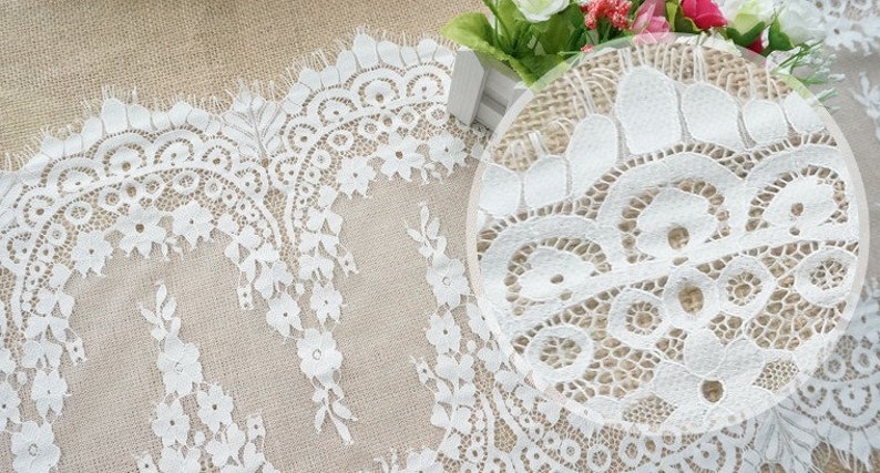 K&ouml;nnte beinhalten: Wei&szlig;e Spitzenborte mit zartem Blumenmuster. Die Spitze hat einen gewellten Rand und ist perfekt, um jedem Projekt einen Hauch von Eleganz zu verleihen.