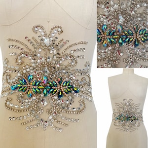 May include: A decorative embellishment featuring a floral design with clear and iridescent green rhinestones. The embellishment is perfect for adding a touch of sparkle to clothing, bags, or other accessories.