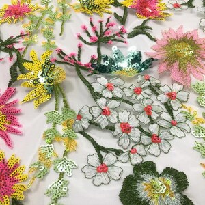 May include: White mesh fabric with embroidered floral designs. The flowers are made of sequins in shades of pink, yellow, and green. The fabric is perfect for crafting, clothing, and home decor.