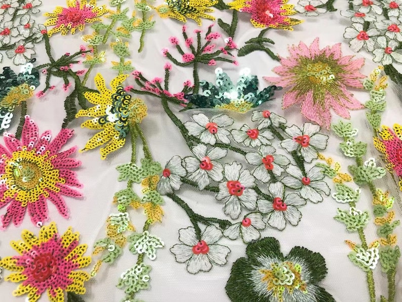May include: White mesh fabric with embroidered floral designs. The flowers are made of sequins in shades of pink, yellow, and green. The fabric is perfect for crafting, clothing, and home decor.