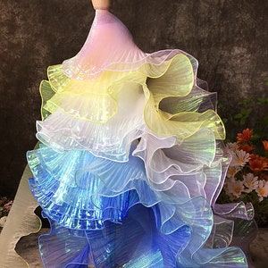 May include: A multi-layered iridescent tulle fabric in shades of pink, yellow, blue, and white. The fabric is pleated and ruffled, creating a dramatic and flowing effect.