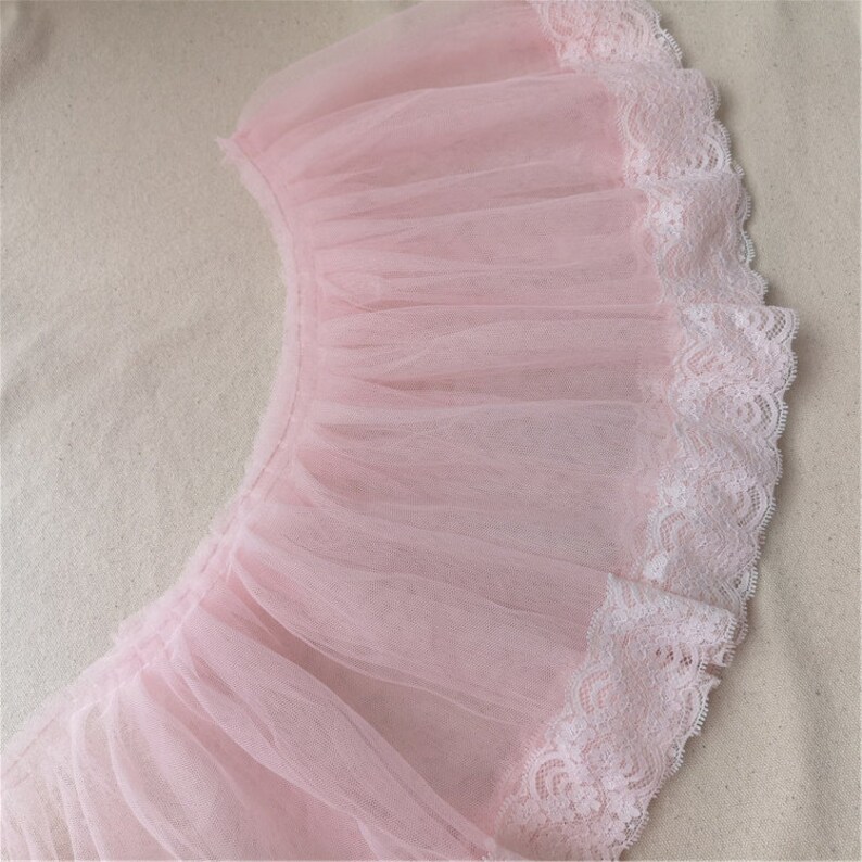 May include: Pink tulle fabric with a white lace trim. The tulle is gathered and ruffled, creating a delicate and feminine look.