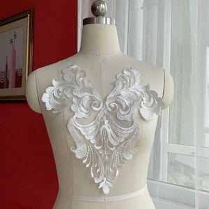 May include: White lace applique featuring a delicate floral design. The applique is ideal for adding a touch of elegance to any garment.