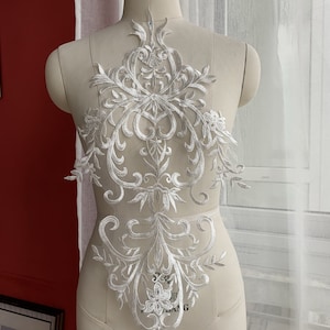 Puede incluir: Aplique de encaje blanco con un diseño floral y de desplazamiento. El aplique está en un maniquí blanco.