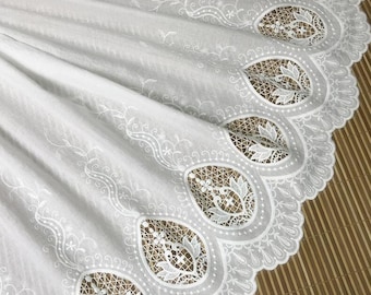 May include: White cotton fabric with a delicate embroidered lace trim. The lace features a repeating pattern of floral motifs and scalloped edges.