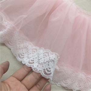 May include: Pink tulle fabric with a white lace trim. The lace has a delicate floral pattern.