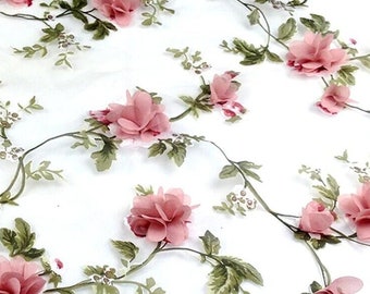 May include: White fabric adorned with a floral design. The pattern showcases pink roses and green leaves, offering a romantic and elegant look. The flowers are spread across the fabric, giving a soft, airy feel.