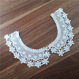 May include: White lace collar with a scalloped edge and delicate floral designs. The collar is ideal for adding a touch of elegance to any garment.