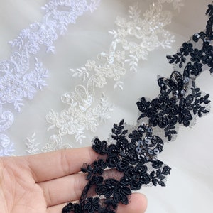 May include: Two white lace trims with floral designs and one black lace trim with floral designs and sequins.