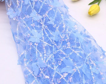 May include: Light blue fabric with a net-like pattern, adorned with sequins and 3D butterfly embellishments. The fabric has a delicate, airy appearance, suitable for crafting or decorative purposes. The butterflies are a lighter shade of blue.