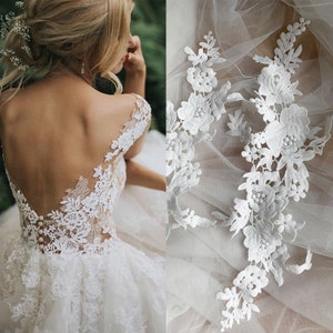 Könnte beinhalten: Ein weißes Spitzen-Hochzeitskleid mit tiefem Rücken und einem transparenten Einsatz. Das Kleid ist mit zarten floralen Spitzenapplikationen verziert. Das Bild zeigt auch eine Nahaufnahme der Spitzenapplikationen.