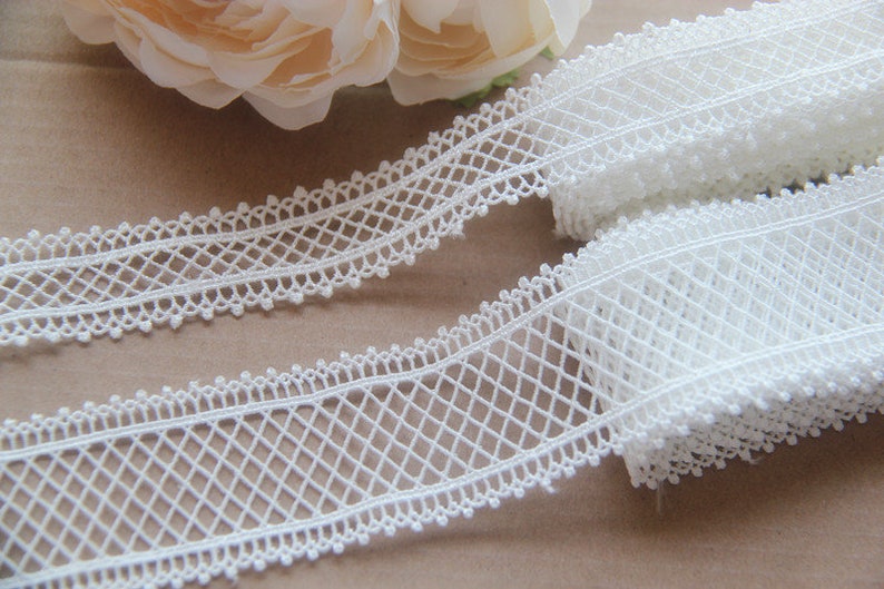 May include: White lace trim with a delicate diamond pattern and scalloped edges. The trim is approximately 2.5 cm wide.
