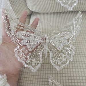 May include: White beaded butterfly applique on a sheer white fabric. The butterfly is made of small white beads and sequins.