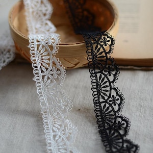 May include: Two spools of delicate lace trim, one white and one black, with a floral pattern. The lace is displayed in a woven basket.