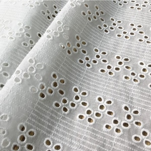 May include: White cotton fabric with a delicate eyelet pattern. The fabric has a subtle sheen and a soft texture.