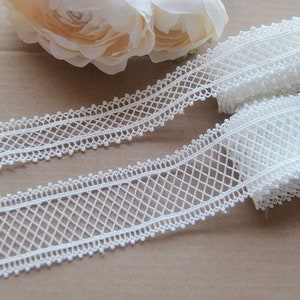 May include: White lace trim with a delicate diamond pattern and small bead accents. The trim is approximately 2.5 cm wide.