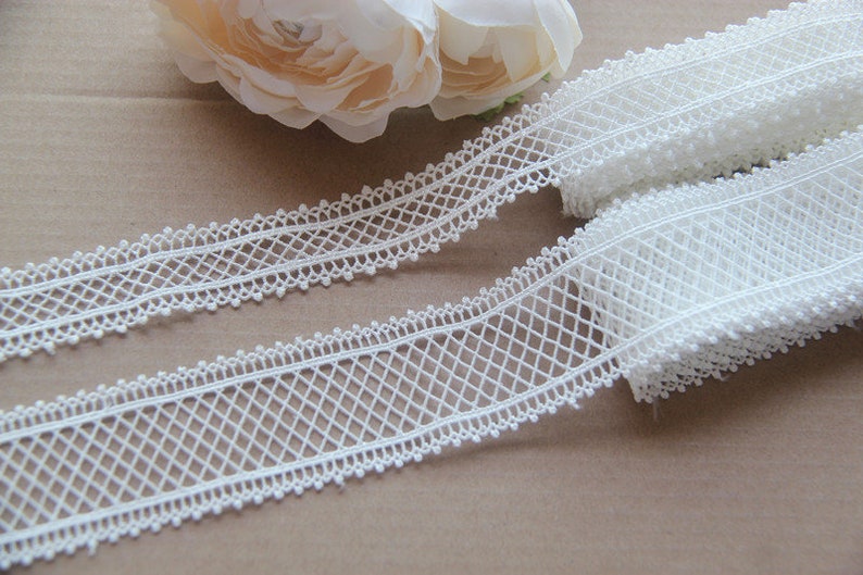 May include: White lace trim with a delicate diamond pattern and small bead accents. The trim is approximately 2.5 cm wide.