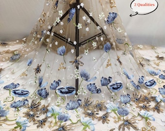 May include: Beige tulle fabric featuring embroidered blue and gold floral designs. The fabric has a delicate, sheer texture and is ideal for creating elegant garments or accessories.