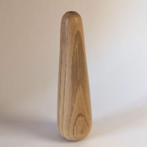 May include: A light-coloured wooden object with a rounded base and a tapered top. The wood grain is visible, and the object has a smooth, polished appearance. The shape is elongated and slightly curved, suggesting a decorative or functional item.