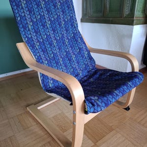 May include: A wooden armchair with a blue patterned cushion and backrest. The cushion features a repeating leaf design in shades of blue and green. The chair has a curved armrest and a light wood frame.