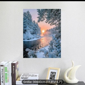 Könnte beinhalten: Eine verschneite Winterlandschaft mit einem Fluss, der sich durch einen Wald schlängelt. Die Sonne geht hinter den Bäumen unter und wirft einen warmen Schein auf den Schnee. Das Bild ist gerahmt und bereit zum Aufhängen an einer Wand.