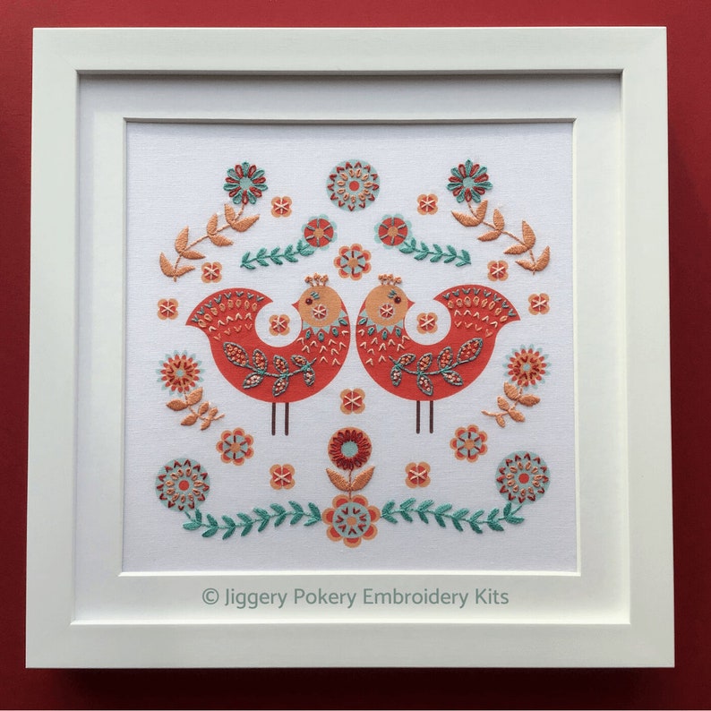 Completed bird embroidery mounted and shown in a square white frame.