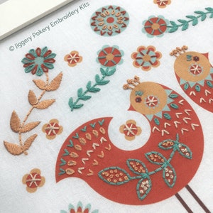 Close up of red Scandi style folk art bird stitched with simple embroidery stitches in turquoise, orange and cream