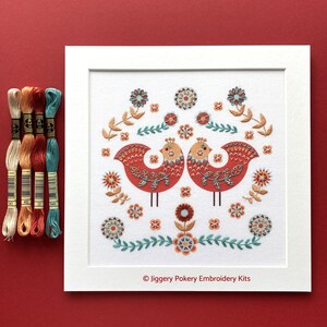 Complete folk art embroidery shown in a white mount with teal, red, apricot and cream DMC threads