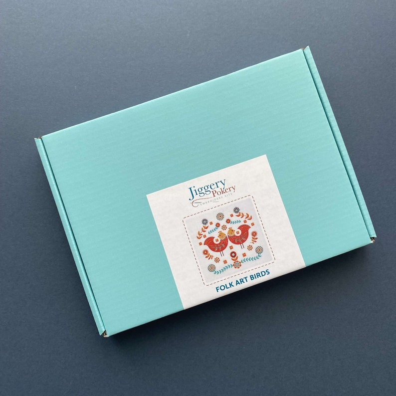 Folk art bird embroidery kit packed into turquoise box with label showing the embroidery design on the outside.