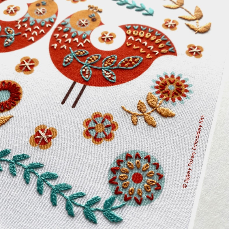 Close up of folk art bird embroidery kit showing embroidered flowers below a red Scandi style bird