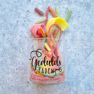 Könnte beinhalten: Ein klares Glasgefäß gefüllt mit bunten Gummibärchen. Das Gefäß hat ein schwarzes Etikett mit der Aufschrift "Gedulds Faden".