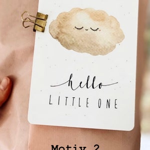 Op de afbeelding: Een witte kaart met een bruine aquarel wolk met een glimlachend gezicht en gesloten ogen. De kaart zegt "hello little one" in zwarte schrift. De kaart is bevestigd aan een bruine papieren zak met een gouden paperclip.