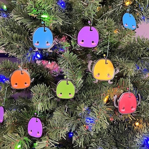 May include: A Christmas tree decorated with colorful ornaments shaped like cartoon characters. The ornaments are in various colors, including red, orange, yellow, green, blue, and purple. Each ornament has a different facial expression.
