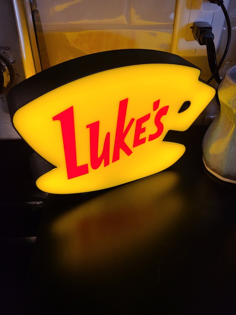 May include: A yellow and red illuminated sign shaped like a coffee cup with the text "Luke's" in red.