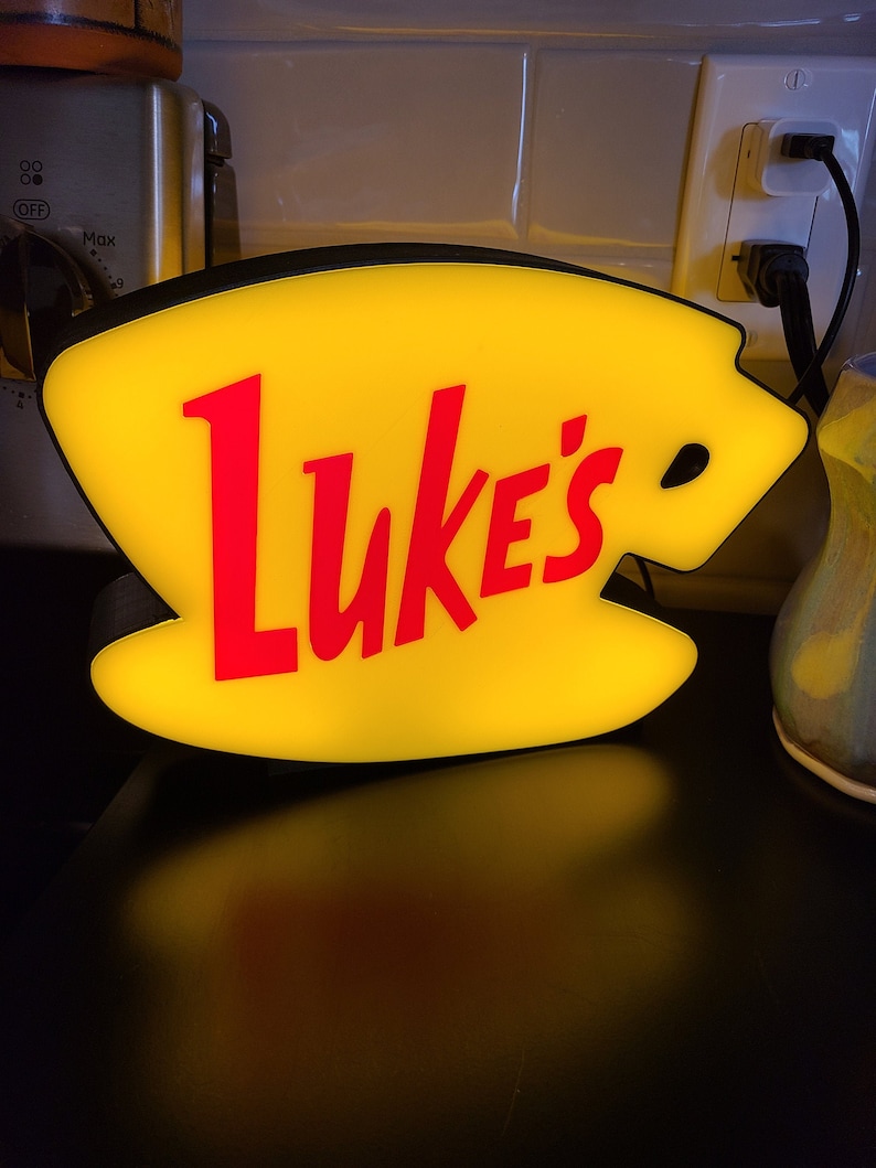 May include: A yellow and red illuminated sign shaped like a coffee cup with the word "Luke's" in red lettering.