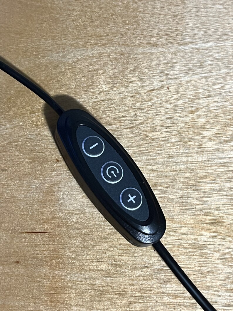 May include: Black remote control with three buttons: a minus sign, a power button with a circle and a plus sign. The remote is connected to a black cord.