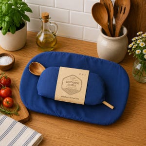 May include: Two solid blue fabric container covers with elastic edges. A tan paper label is wrapped around the smaller cover, featuring the text "CONTAINER COVERS PLASTIC FREE" and "9" X 13"" along with "HANDMADE IN MINNESOTA".