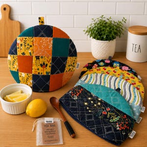Pode incluir: Uma capa para bule redonda e acolchoada com um patchwork de tecido amarelo mostarda, azul escuro e azul-petróleo com padrões florais e geométricos. Uma pilha de capas semelhantes está ao lado, junto a uma pequena taça com fatias de limão.